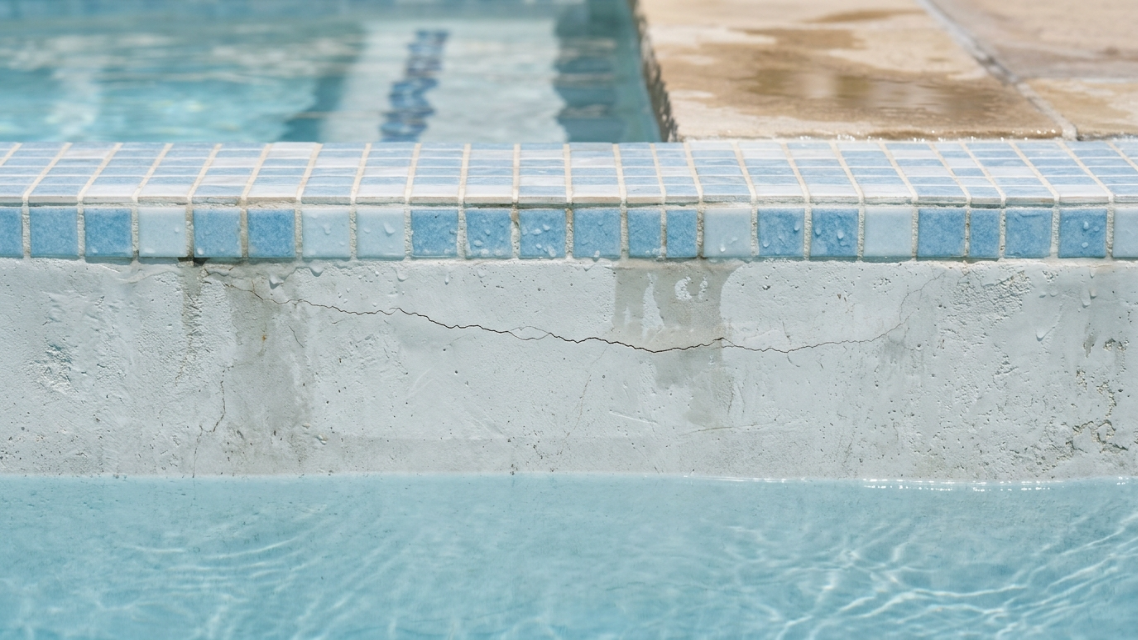 Pool Crack Repair Cost Guide: Close-up of a hairline crack running along a pool's plaster surface near the waterline