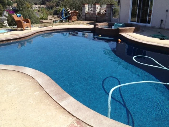 Pool with an attached raised spa and patio chairs on the deck